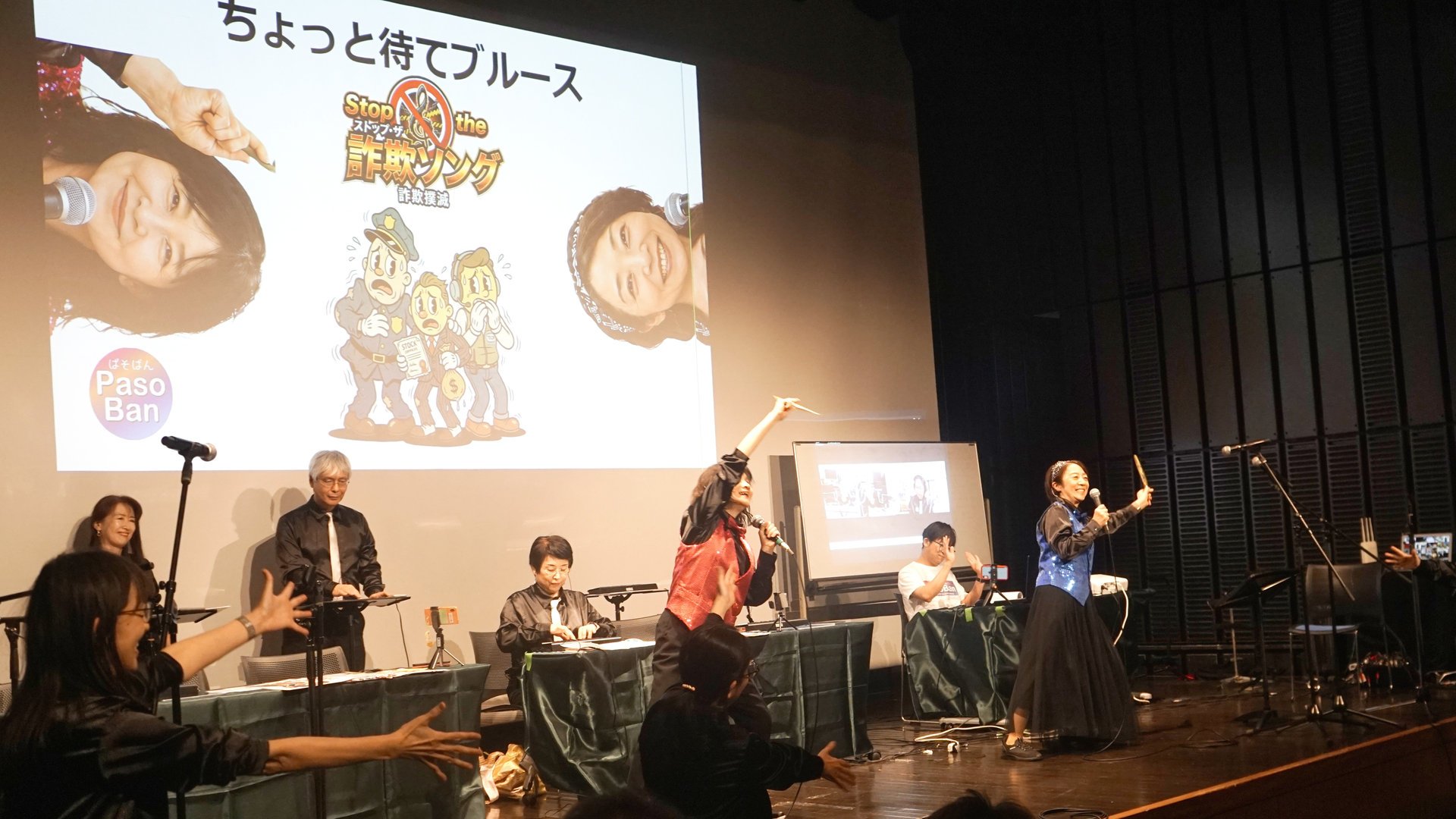 舞台で歌う出演者と、手を上げて参加する会場の様子。